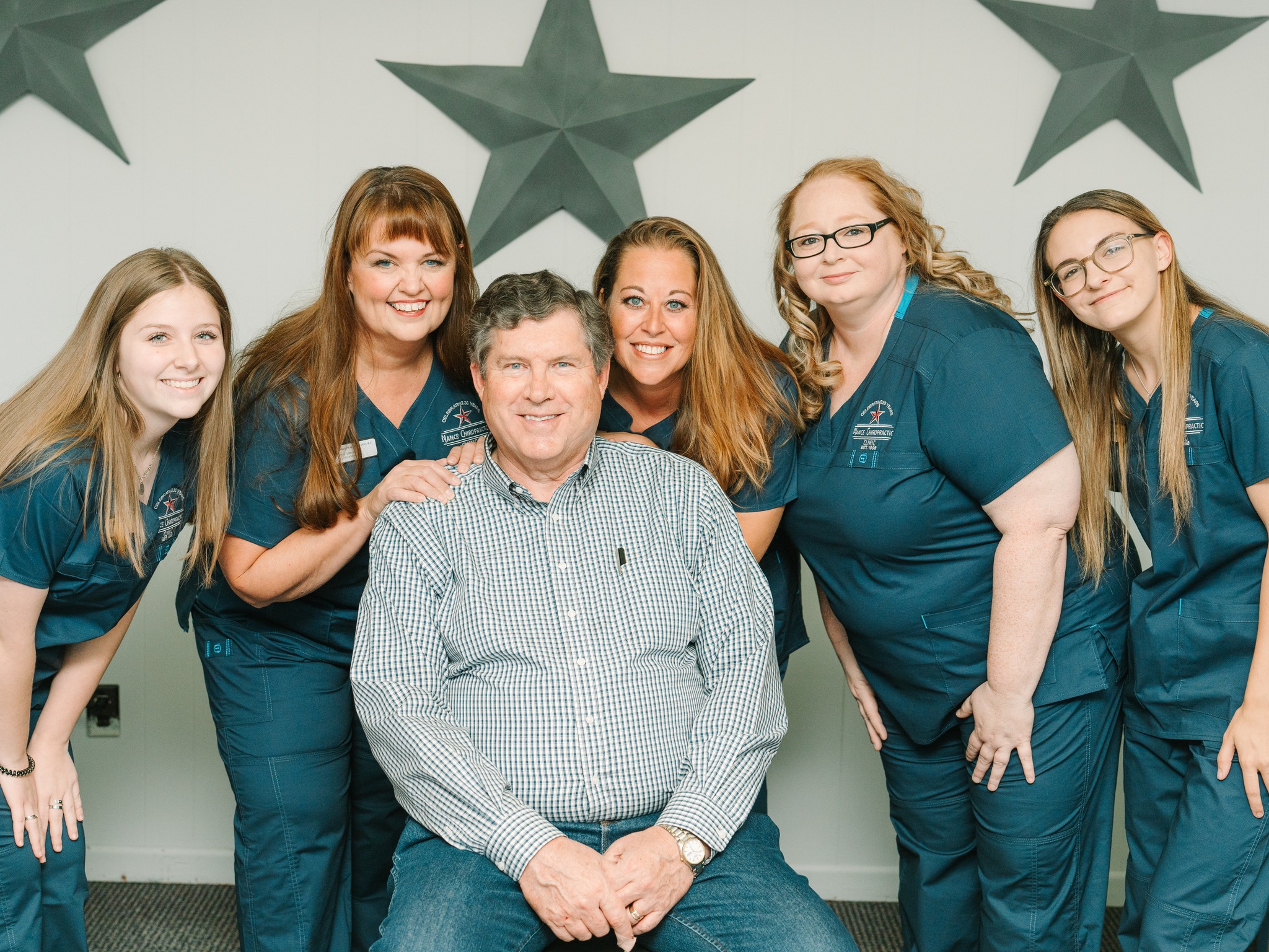Dr. Jerry C. Nance and the full Nance Chiropractic Clinic staff in Stephenville, TX — Dr. Nance seated, surrounded by team members in teal Nance Chiropractic scrubs